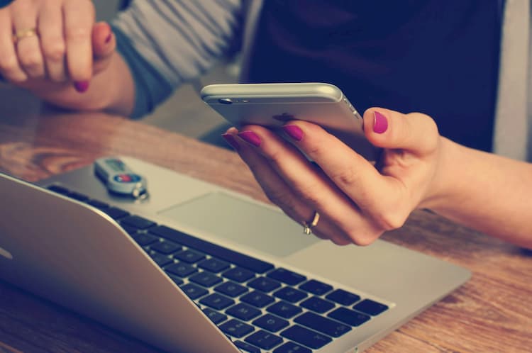 Woman at laptop holding mobile phone